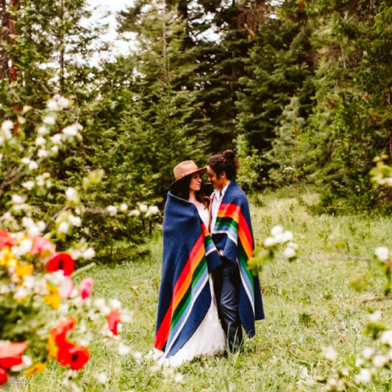 wedding couple wrapped in colorful blanket in meadow next to forest